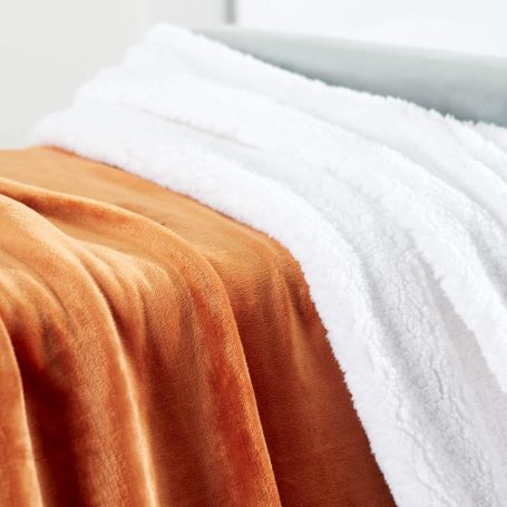 Reversible throw blanket with one side burnt orange and the other side crisp white, folded on a bed for a warm fall accent
